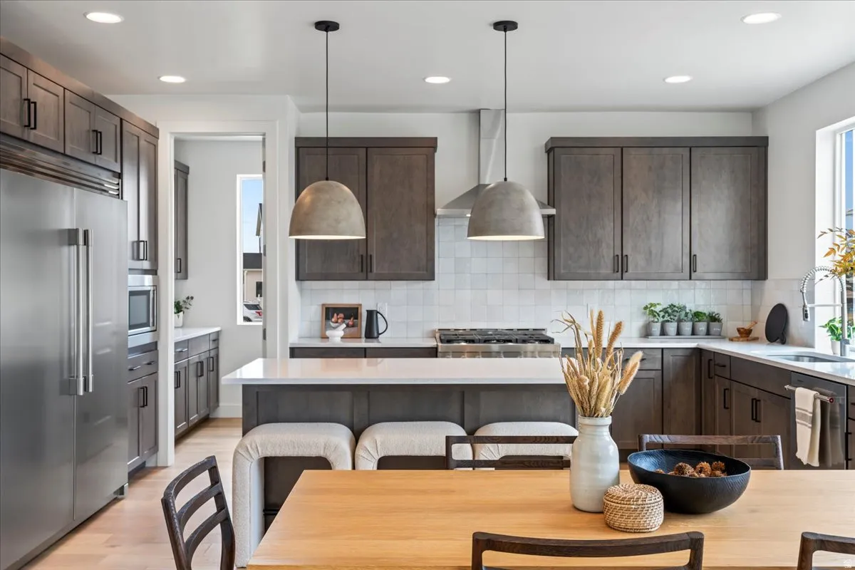 Kitchen featuring built in appliances, dark wood finish cabinetry, light wood-style flooring, and pendant lighting