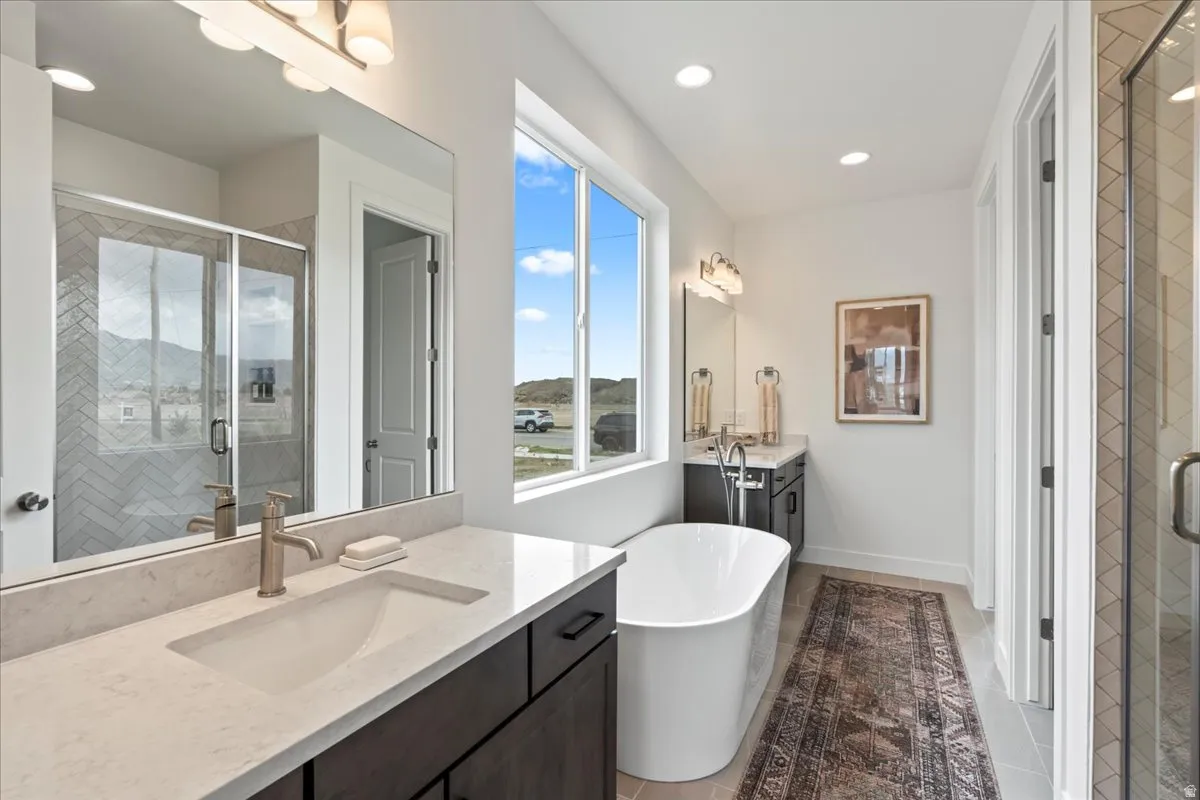 Primary bathroom featuring two vanities, a stall shower, a freestanding tub, light tile patterned floors, and recessed lighting