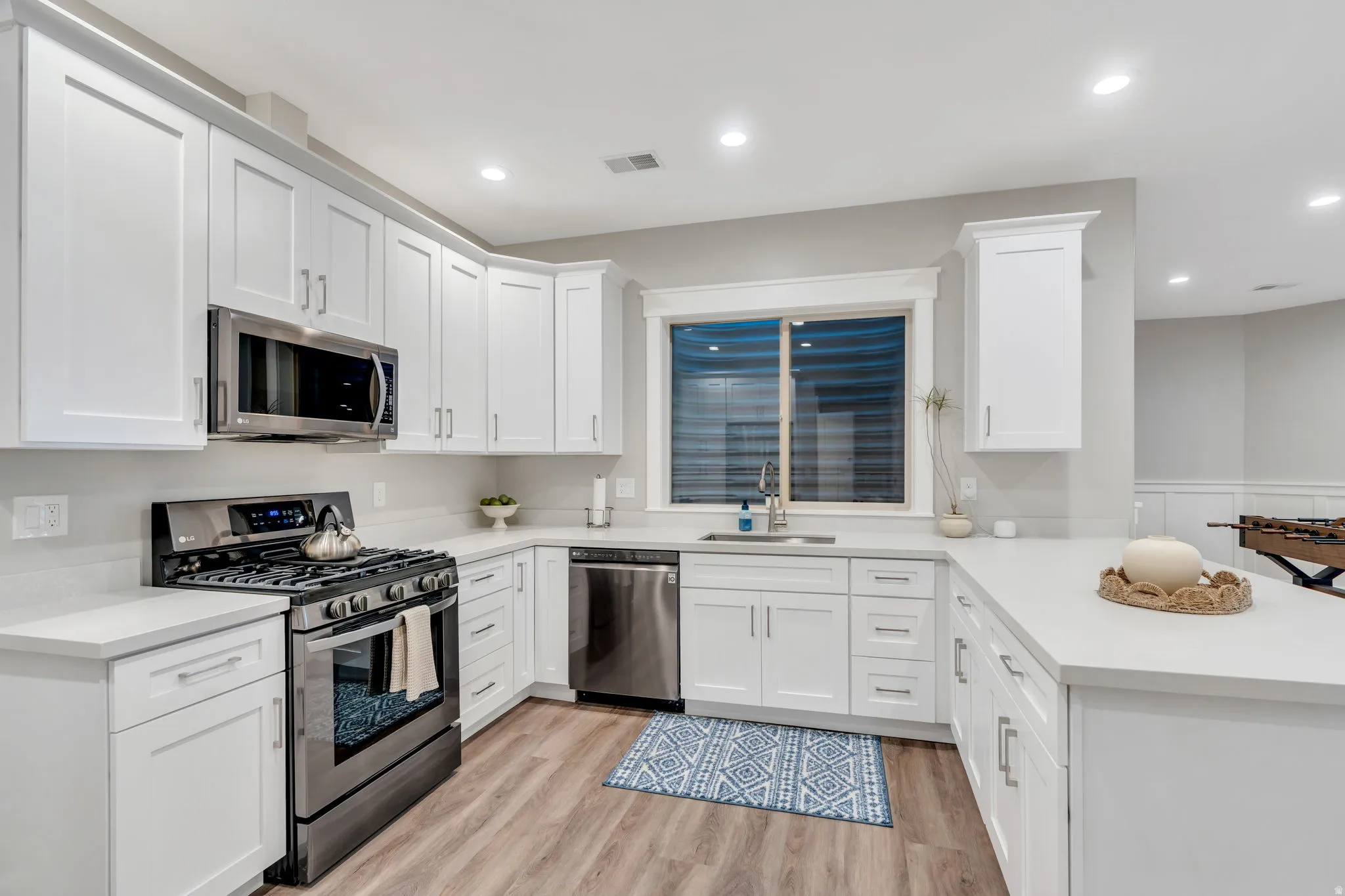 Downstairs Kitchen with stainless steel appliances, LVP flooring, a breakfast bar, white cabinetry, and recessed lighting
