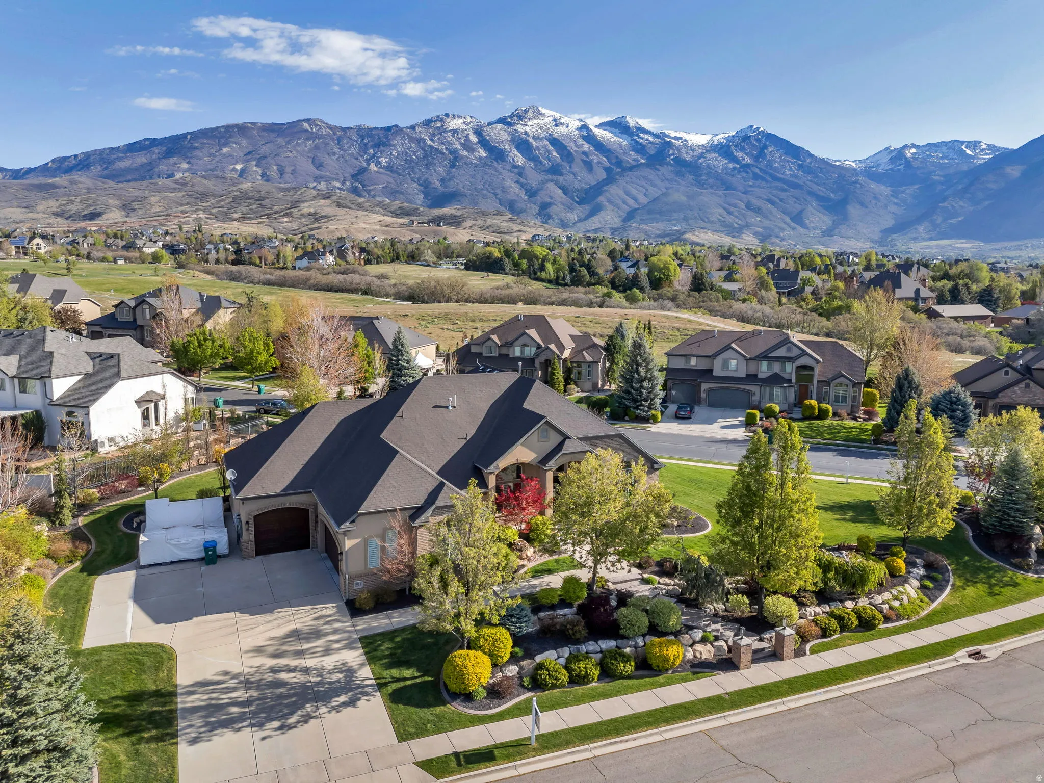Expansive residential property with a multi-level roofline, featuring mature landscaping, a stone retaining wall, and a concrete driveway
