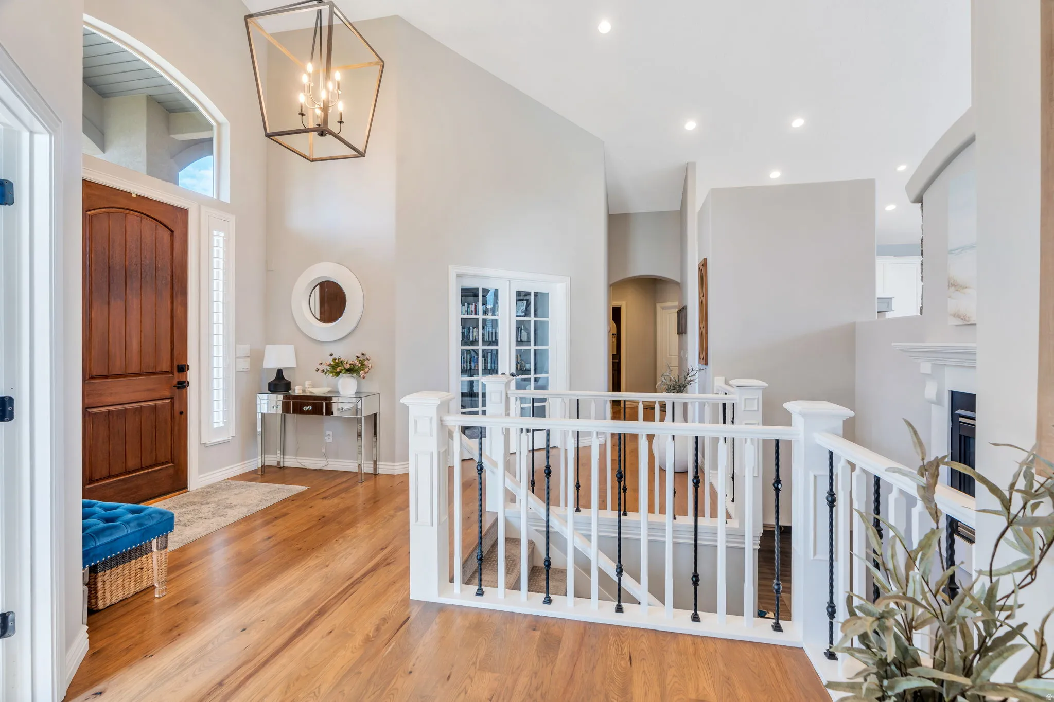 Grand entry foyer featuring a solid wood door with an arched transom, wood-finish flooring, a contemporary chandelier, and a white balustrade staircase with black iron spindles