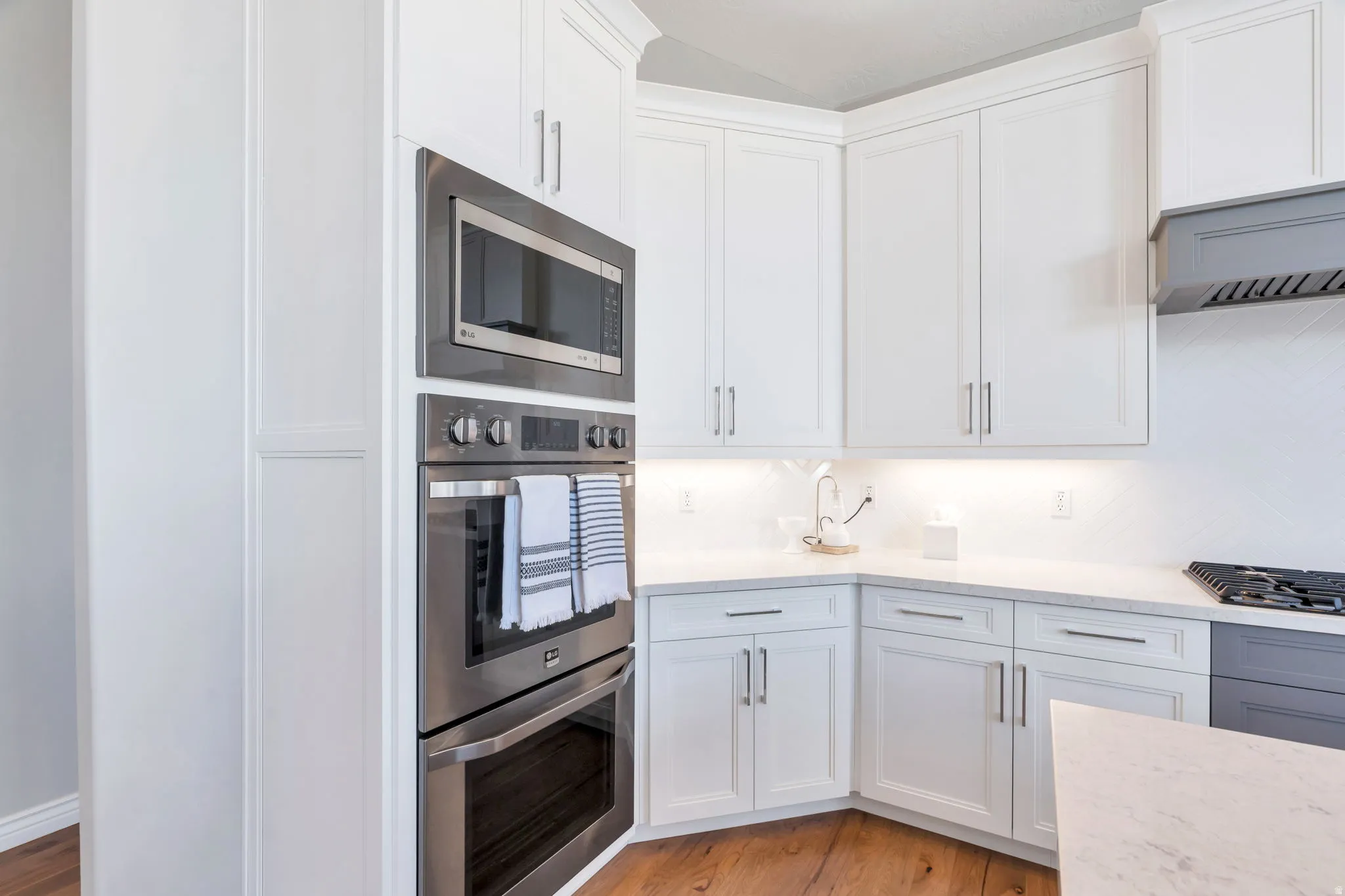 Kitchen featuring stainless steel appliances, custom cabinetry, quartz countertops, and hardwood floors