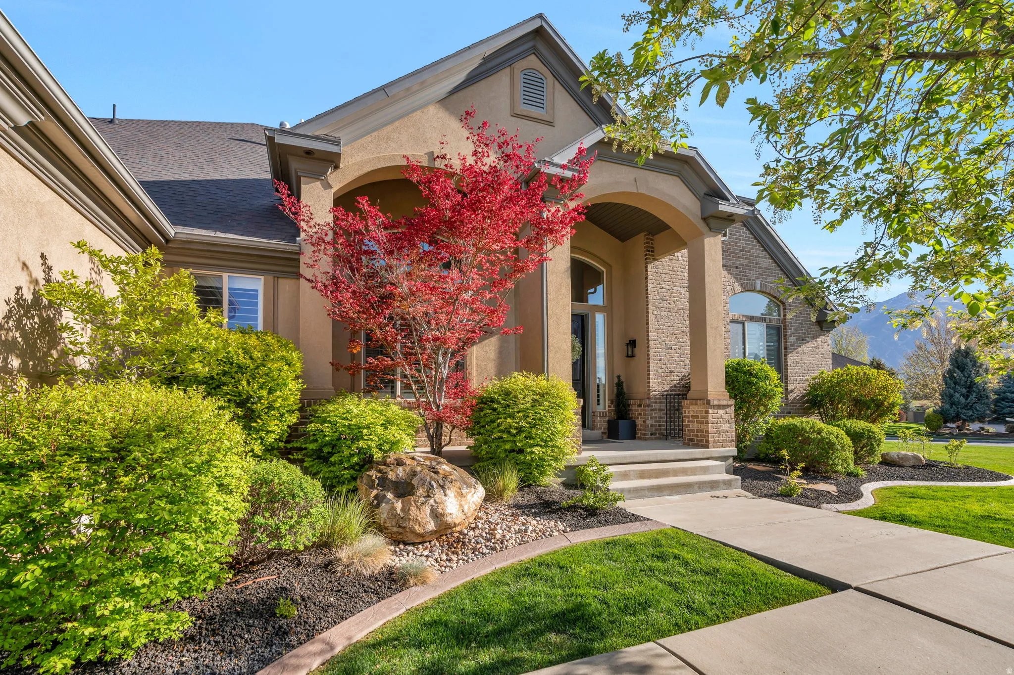 Stucco and stone exterior featuring a covered porch entry, arched columns, and a concrete walkway
