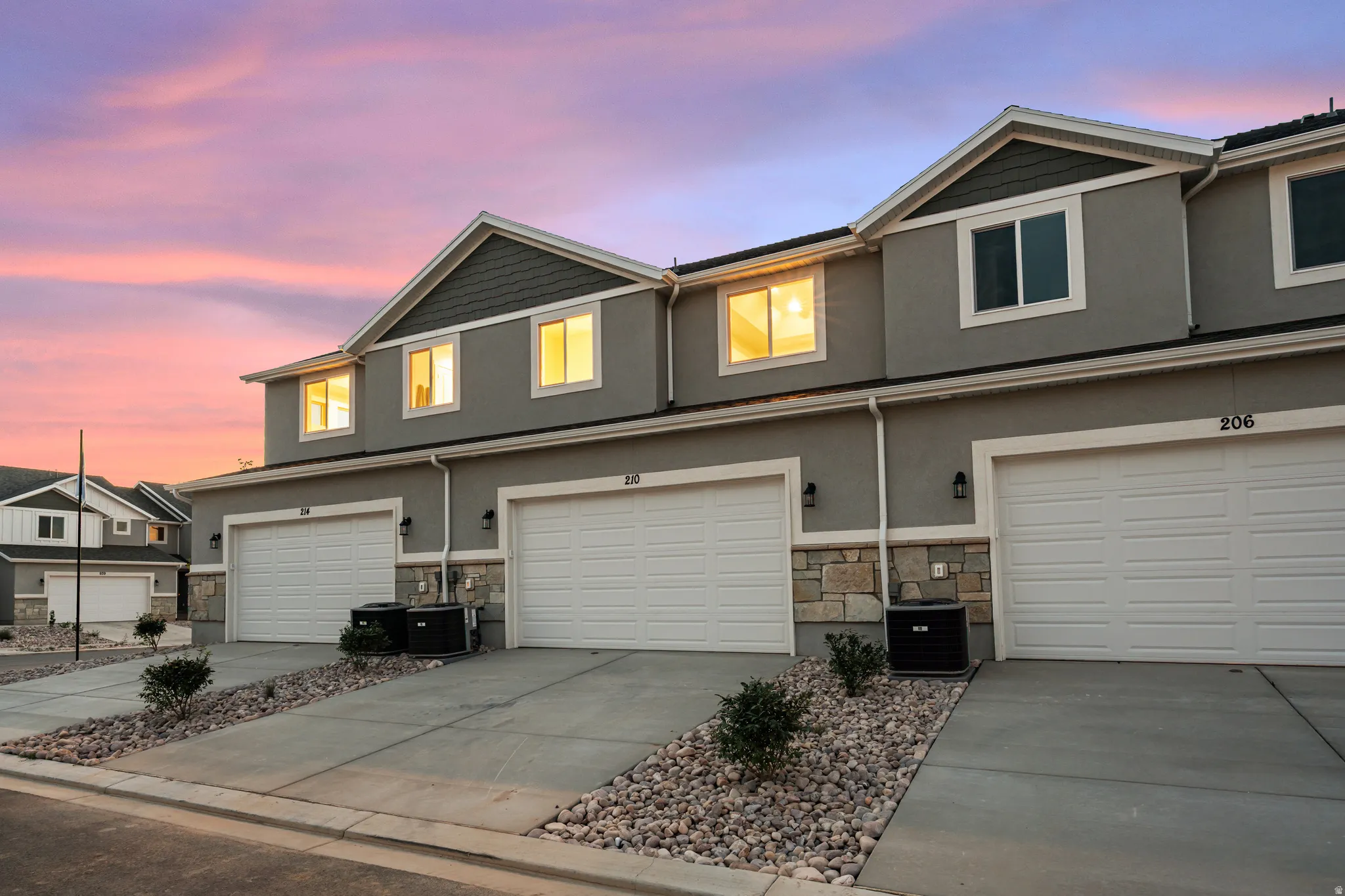 Contemporary townhome exterior featuring gray stucco siding, stone accents, white trim, and a two-car garage