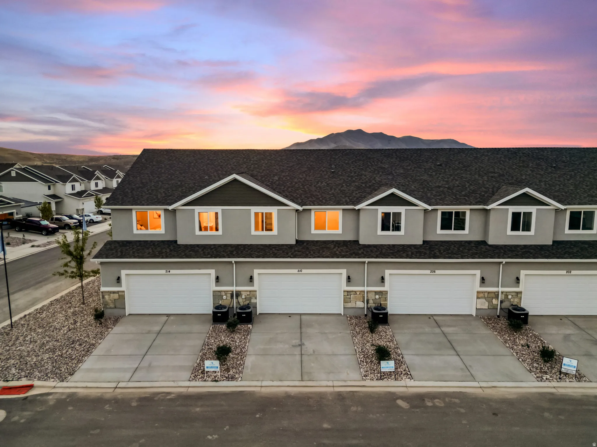 Row of contemporary townhomes featuring gray siding, stone accents, individual garages with white doors, and paved driveways