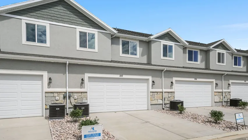 Contemporary townhome exterior featuring light gray stucco, white trim, and a stone facade accent