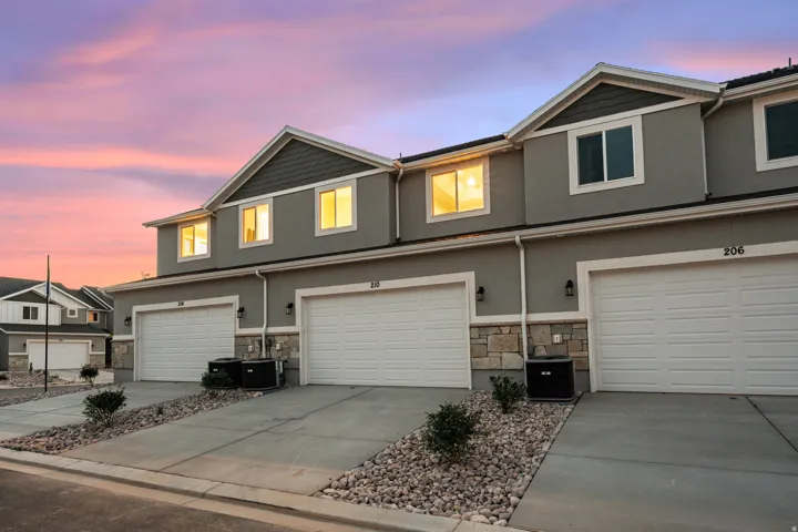 Contemporary townhome exterior featuring gray stucco siding, stone accents, white trim, and a two-car garage