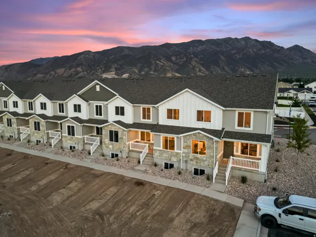 Townhome exterior featuring stone accents, white railings, dark shingles, and a mountainous backdrop