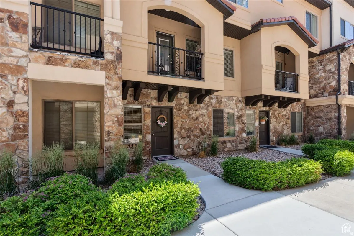 View of front of property featuring a balcony, stone siding, and stucco siding