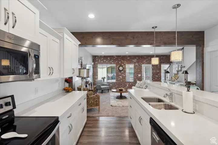 Kitchen with stainless steel appliances, white cabinets, pendant lighting, light stone countertops, and open floor plan