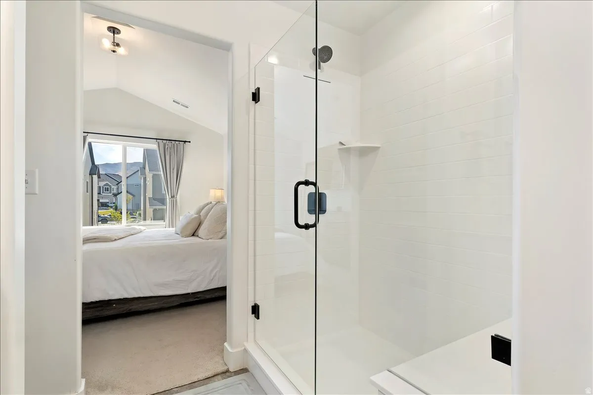 Ensuite bathroom with a shower stall, vaulted ceiling, and light colored carpet