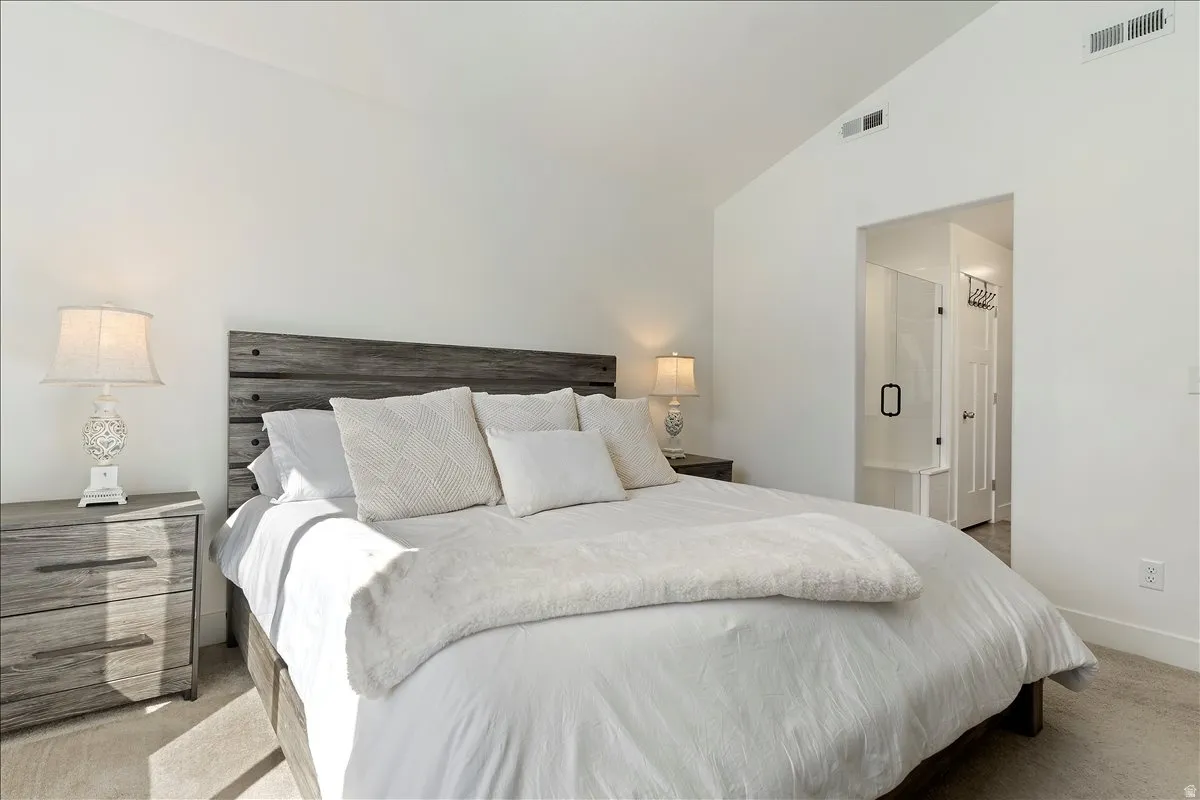 Bedroom featuring lofted ceiling, light carpet, and ensuite bathroom