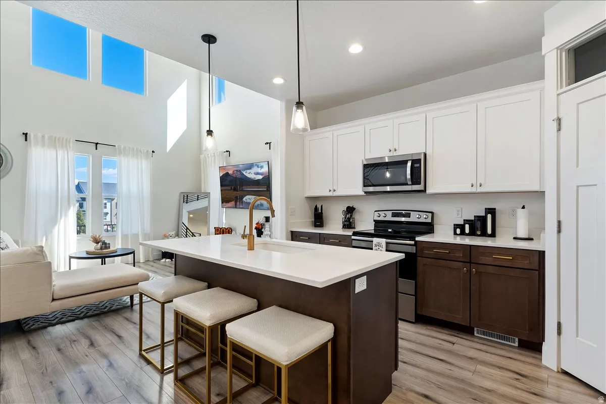 Two tone kitchen featuring two tone color scheme, stainless steel appliances, a kitchen bar, open floor plan, and a high ceiling