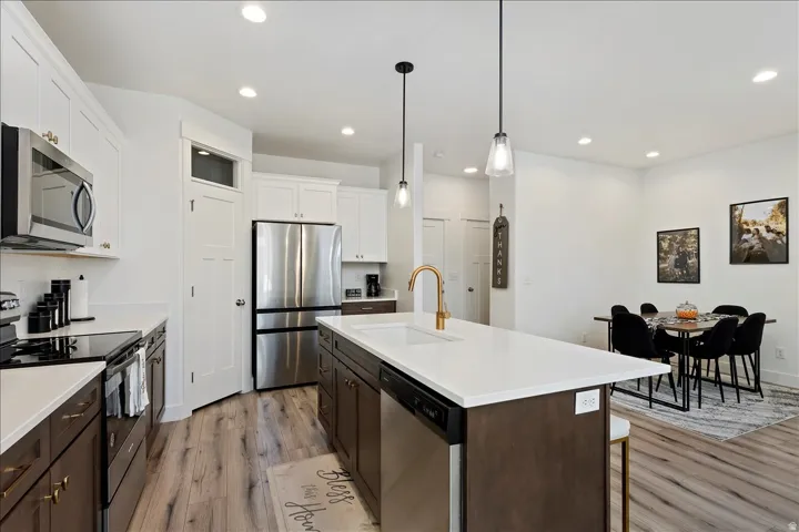 Dual tone kitchen with stainless steel appliances, two tone cabinetry, light wood-style floors, an island with sink, and decorative light fixtures