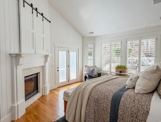 Master Bedroom featuring lofted ceiling, access to exterior, light wood-type flooring, a barn door, and a glass covered fireplace