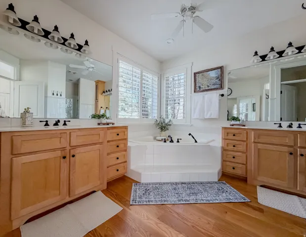 Full Master bath with ceiling fan, two vanities, a bath, light wood-style flooring, and a shower stall