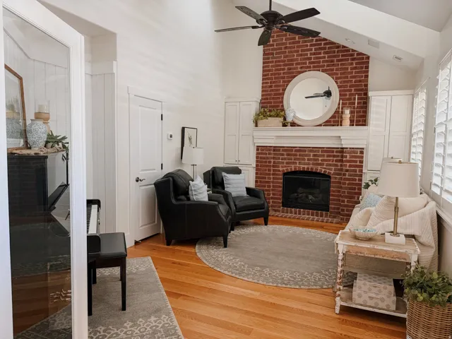 Living room featuring light wood-style floors, a brick fireplace, a ceiling fan, and lofted ceiling