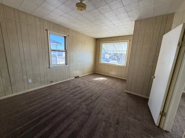 Unfurnished room with dark colored carpet and wood walls