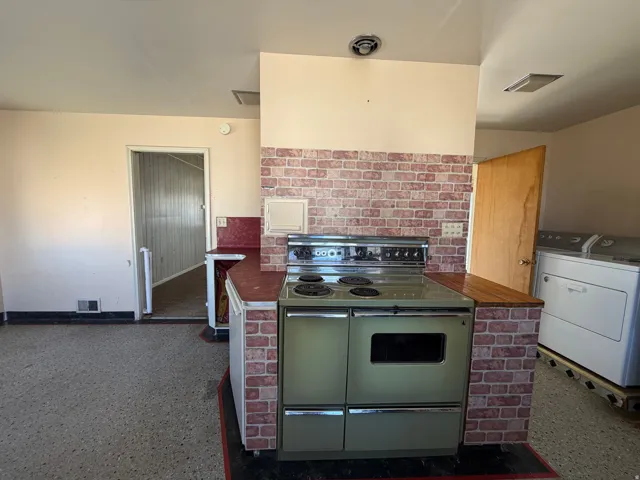 Kitchen featuring range with two ovens, washer / clothes dryer, light aggregate flooring, and dark countertops