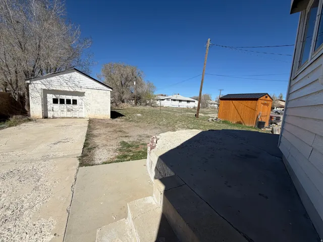 View of yard with driveway, a patio area, a storage shed, and a garage