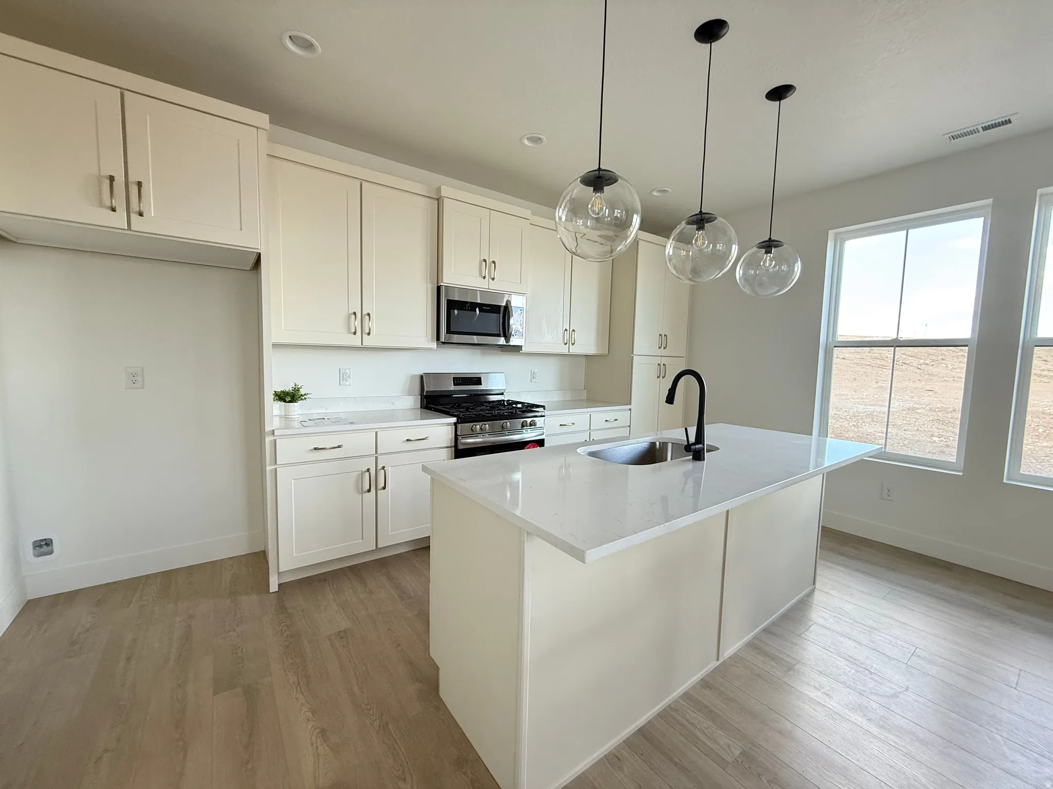 Kitchen featuring stainless steel appliances, light wood-style floors, a kitchen island with sink, pendant lighting, and white cabinets