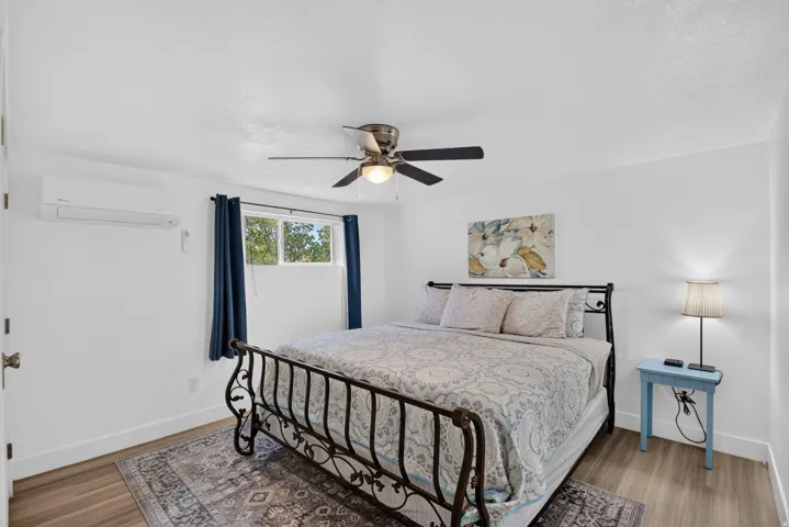 Unit 2A: Wood-finish flooring, ceiling fan with integrated lighting, wall-mounted air conditioning unit, and a window with blinds