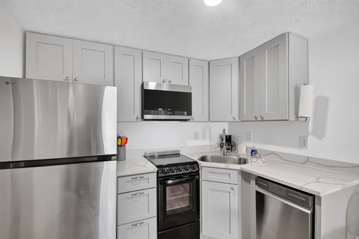 Unit 2A: Kitchen with light gray cabinetry, stainless steel appliances, corner sink, and light-toned countertops