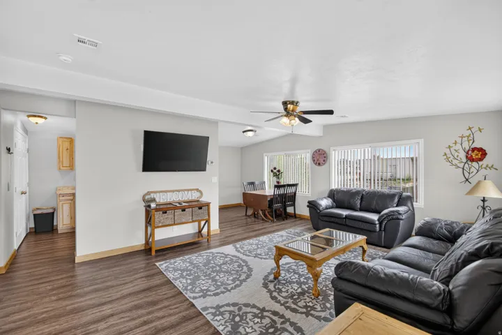 Unit 3: Wood-finish flooring throughout, light gray wall tones, ceiling fan with integrated lighting, multiple windows with vertical blinds, and a built-in wall-mounted television