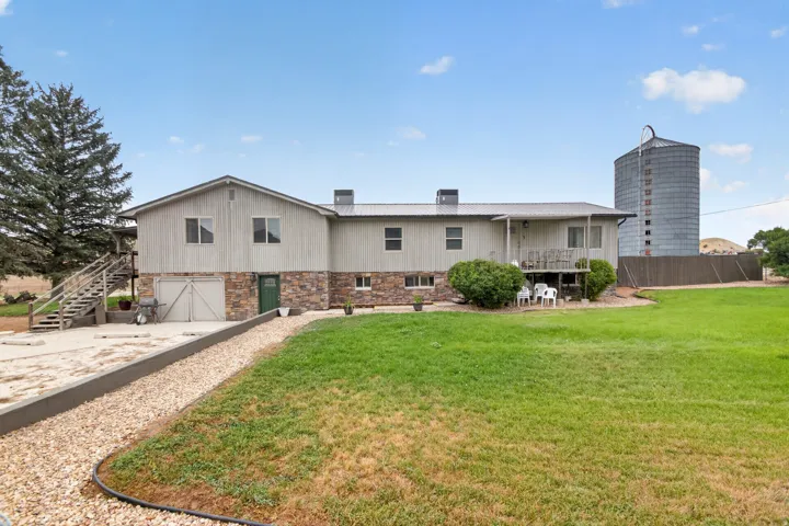 Exterior featuring vertical siding and stone accents, a metal roof, a full-length deck, and an expansive lawn