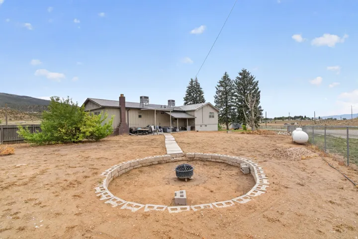 Expansive backyard featuring a stone block fire pit, concrete paver pathway, and mature trees