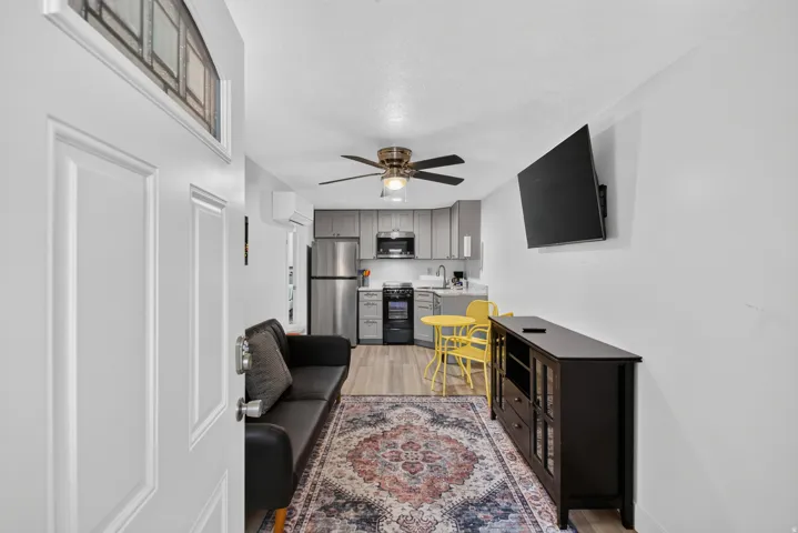 Unit 2A: Compact living space featuring wood-finish flooring, a ceiling fan, gray cabinetry, stainless steel appliances, and a wall-mounted display
