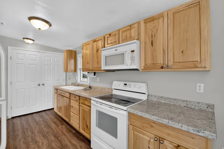 Unit 3: Kitchen featuring wood-finish cabinetry, light-toned countertops, a white electric range, an over-range microwave, and wood-finish flooring