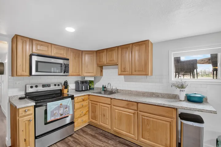 Unit 2B: Corner kitchen featuring wood-finish cabinetry, stainless steel appliances, speckled countertops, and a white subway tile backsplash