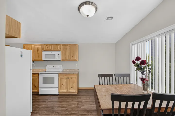 Unit 3: Kitchen and dining area featuring wood-finish flooring, light wood cabinetry, white appliances, and a window with vertical blinds