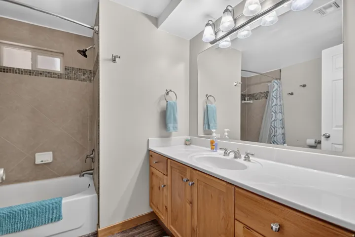 Unit 3: Full bathroom featuring a white tub, tiled shower surround with mosaic accent, and a light wood-finish vanity with a single basin and white countertop