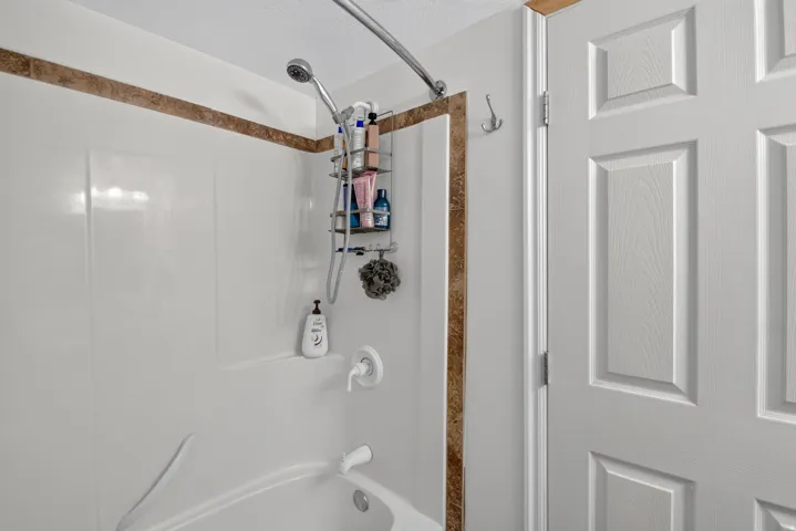 Unit 2B: White panel door, white shower/tub combination, and a decorative tile accent band