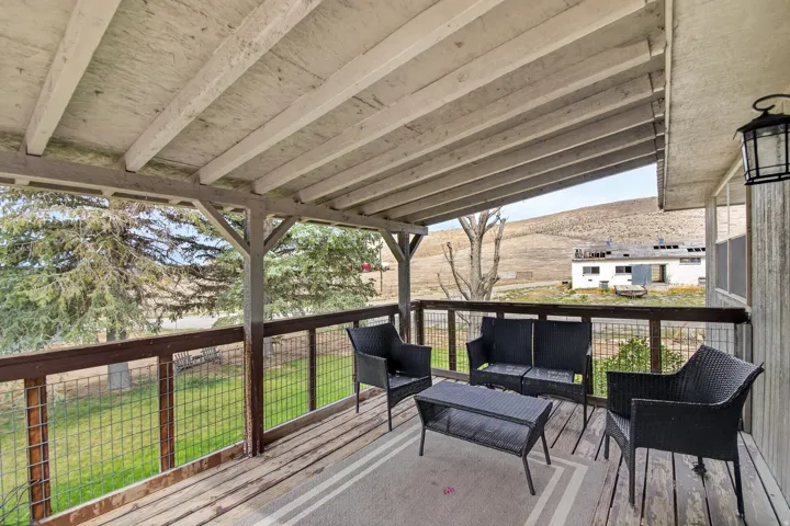 Unit 1: Covered porch featuring wood decking, wood railing with mesh infill, exposed ceiling beams, and an exterior wall lantern