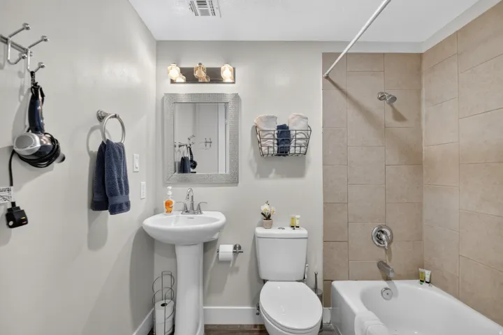 Unit 1: Pedestal sink with chrome faucet, a recessed medicine cabinet, and a bathtub with a shower featuring tan tiled walls