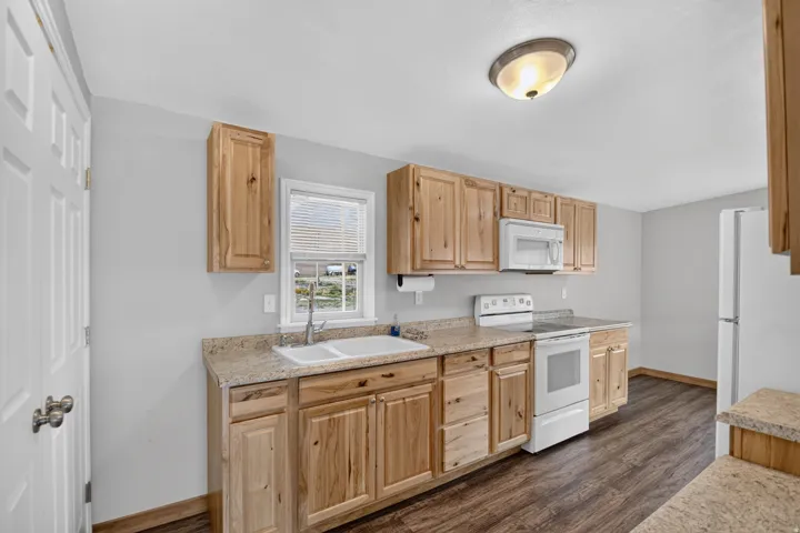 Unit 3: Kitchen featuring wood-finish cabinetry, light-toned countertops, a double basin sink, and white appliances