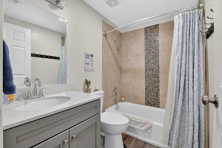 Unit 1: Bathroom featuring a vanity with a white countertop and undermount sink, a chrome faucet, a tub with a shower fixture, and a tiled shower surround with a mosaic accent strip