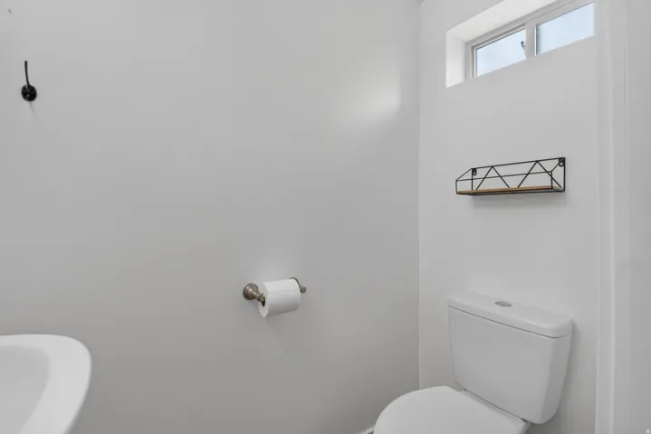 Unit 2B: White toilet with a built-in cistern, a wall-mounted sink, and a decorative wall shelf