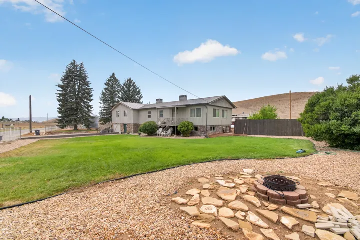 Spacious backyard featuring a manicured lawn, established trees, and a stone-lined fire pit