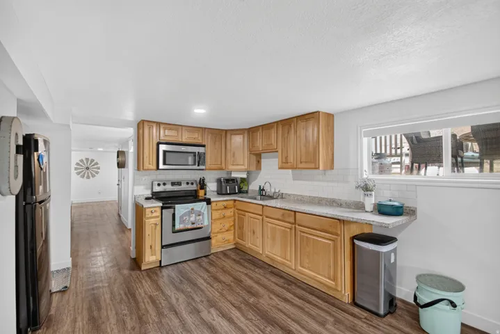 Unit 2B: Wood-finish flooring, light wood cabinetry, stainless steel appliances, white subway tile backsplash, and light-toned countertops