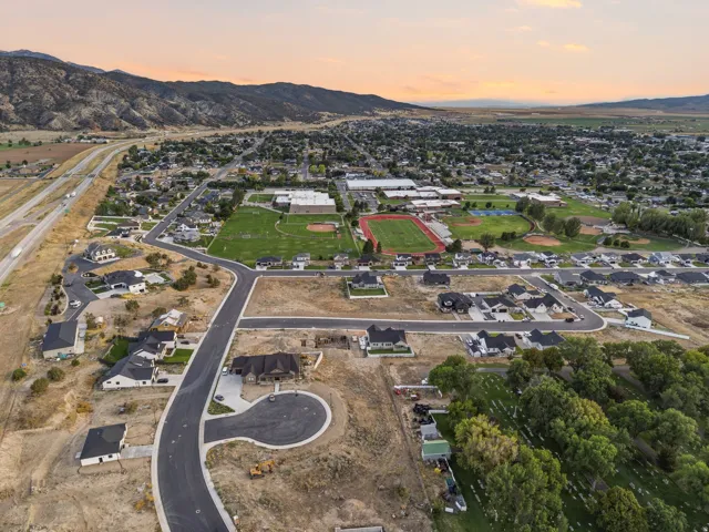 New construction homes situated on a developing street, with visible athletic fields and mountainous terrain