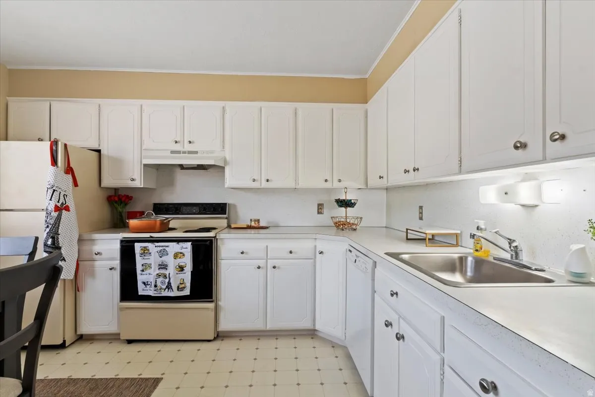 Kitchen featuring light flooring, white appliances, white cabinets, light countertops, and crown molding