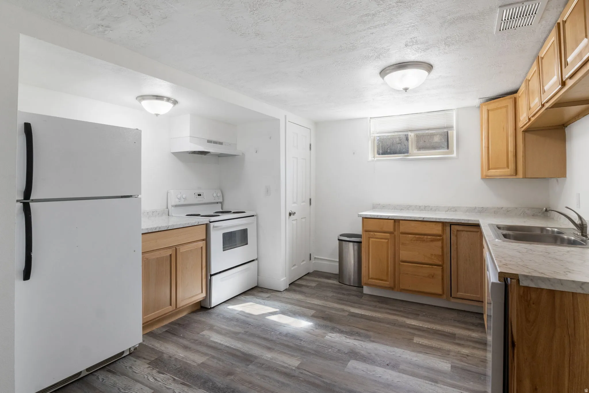 Kitchen featuring white appliances, light countertops, dark vinyl floors, a textured ceiling, and light wood finish cabinets
