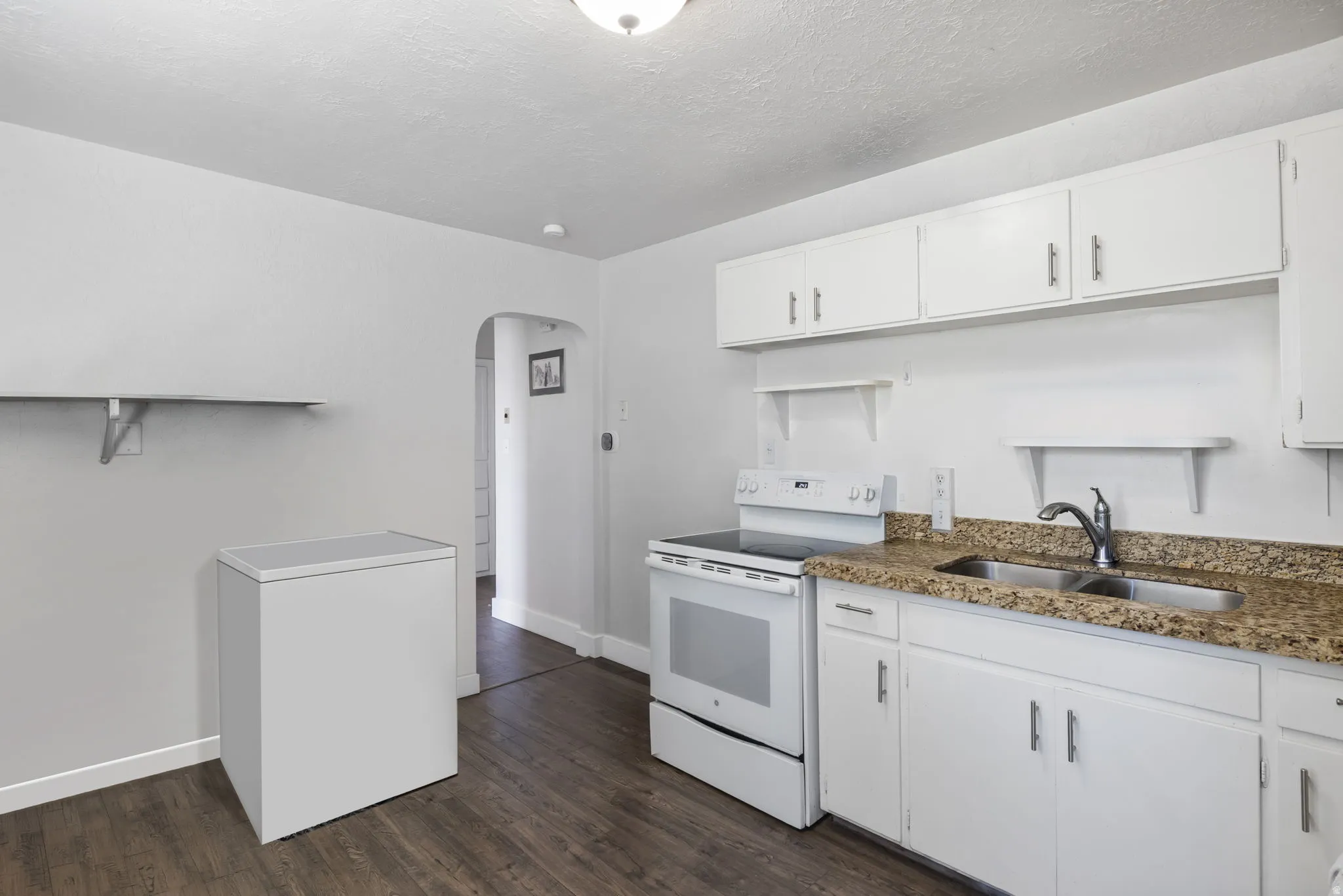 Kitchen with arched walkways, white appliances, white cabinetry, dark wood finished floors, and dark stone countertops