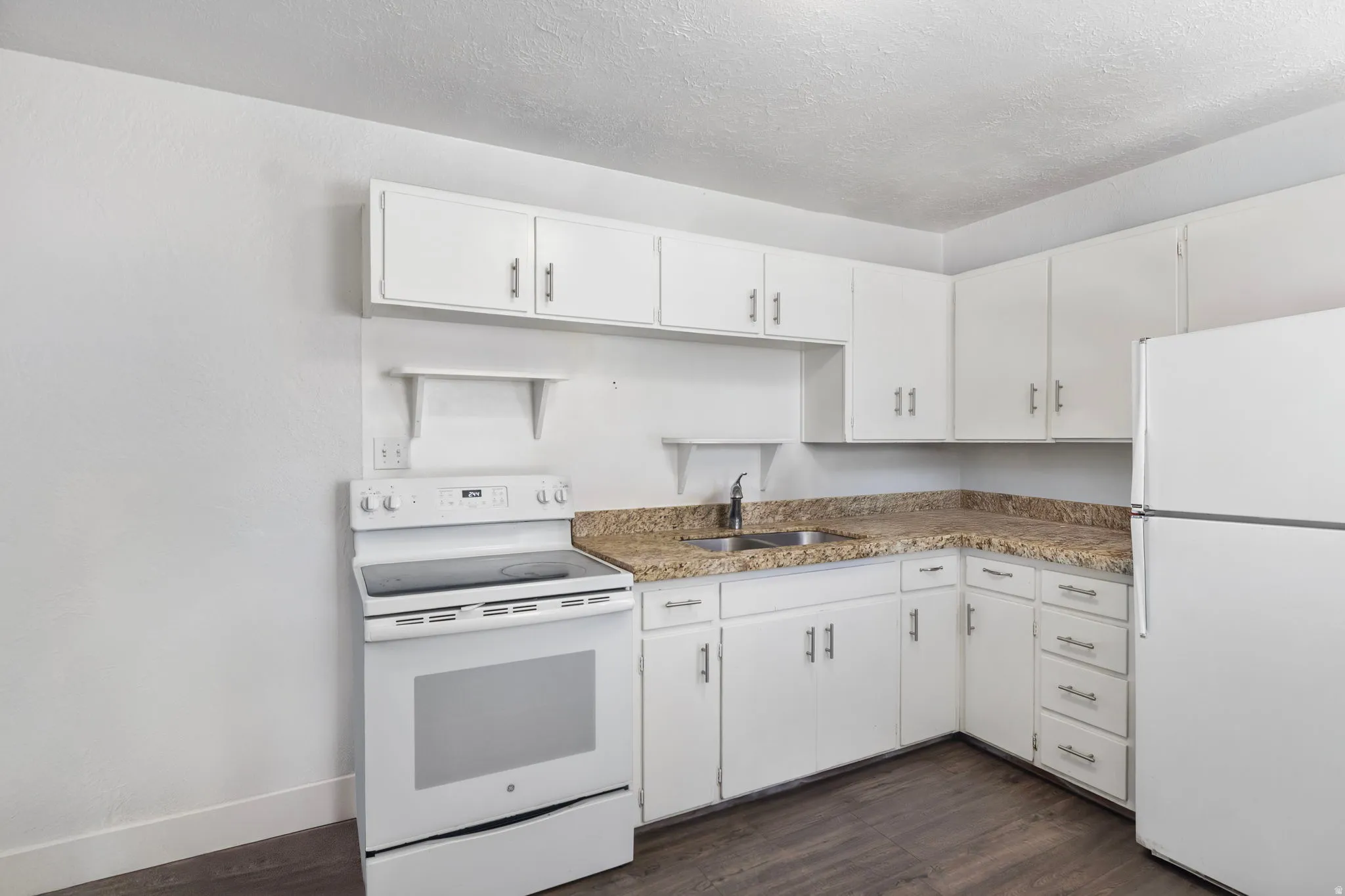 Kitchen with white appliances, white cabinets, dark wood-type flooring, a textured ceiling, and light countertops