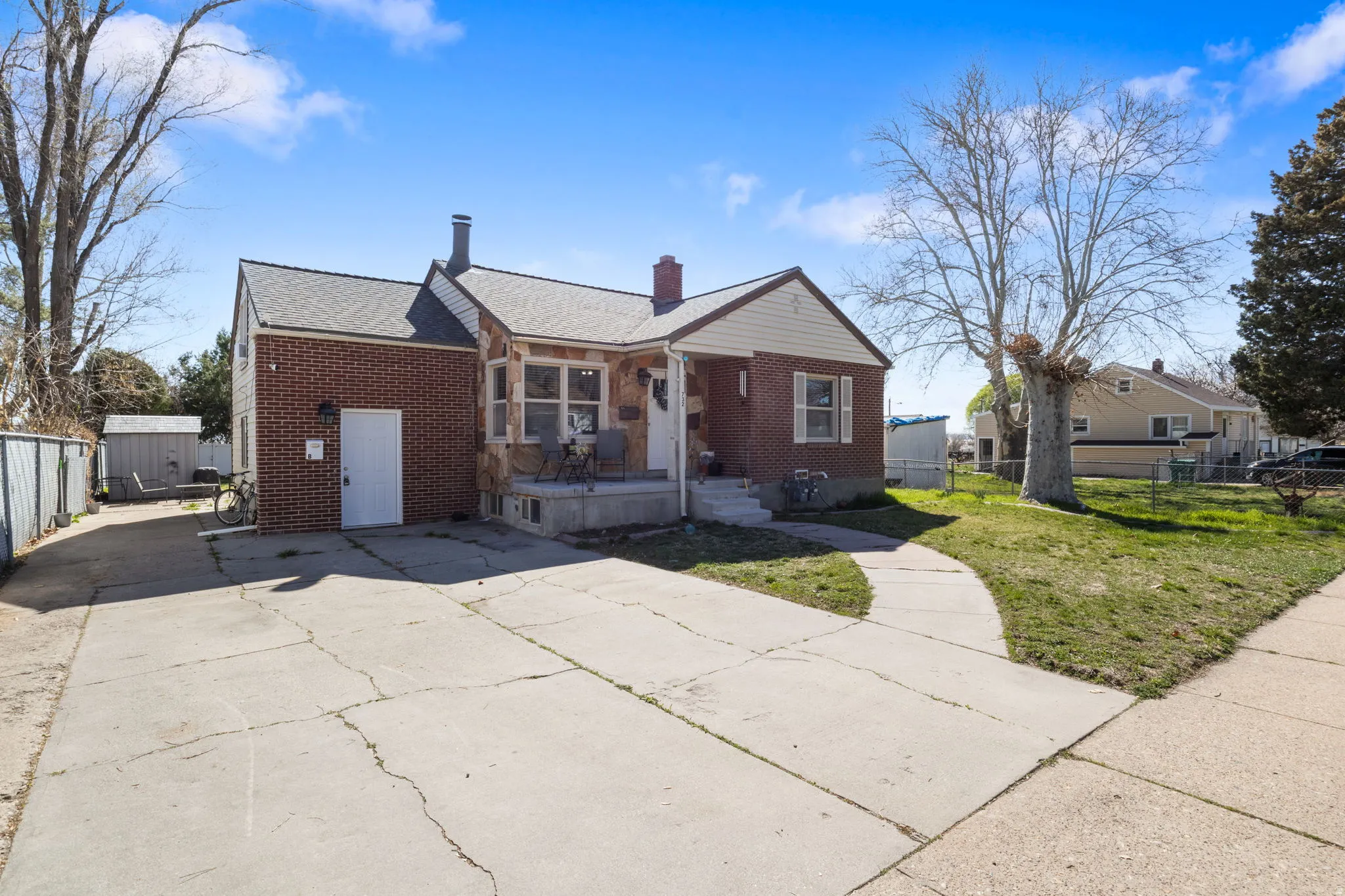 Bungalow featuring brick siding, a chimney, driveway, and a shingled roof