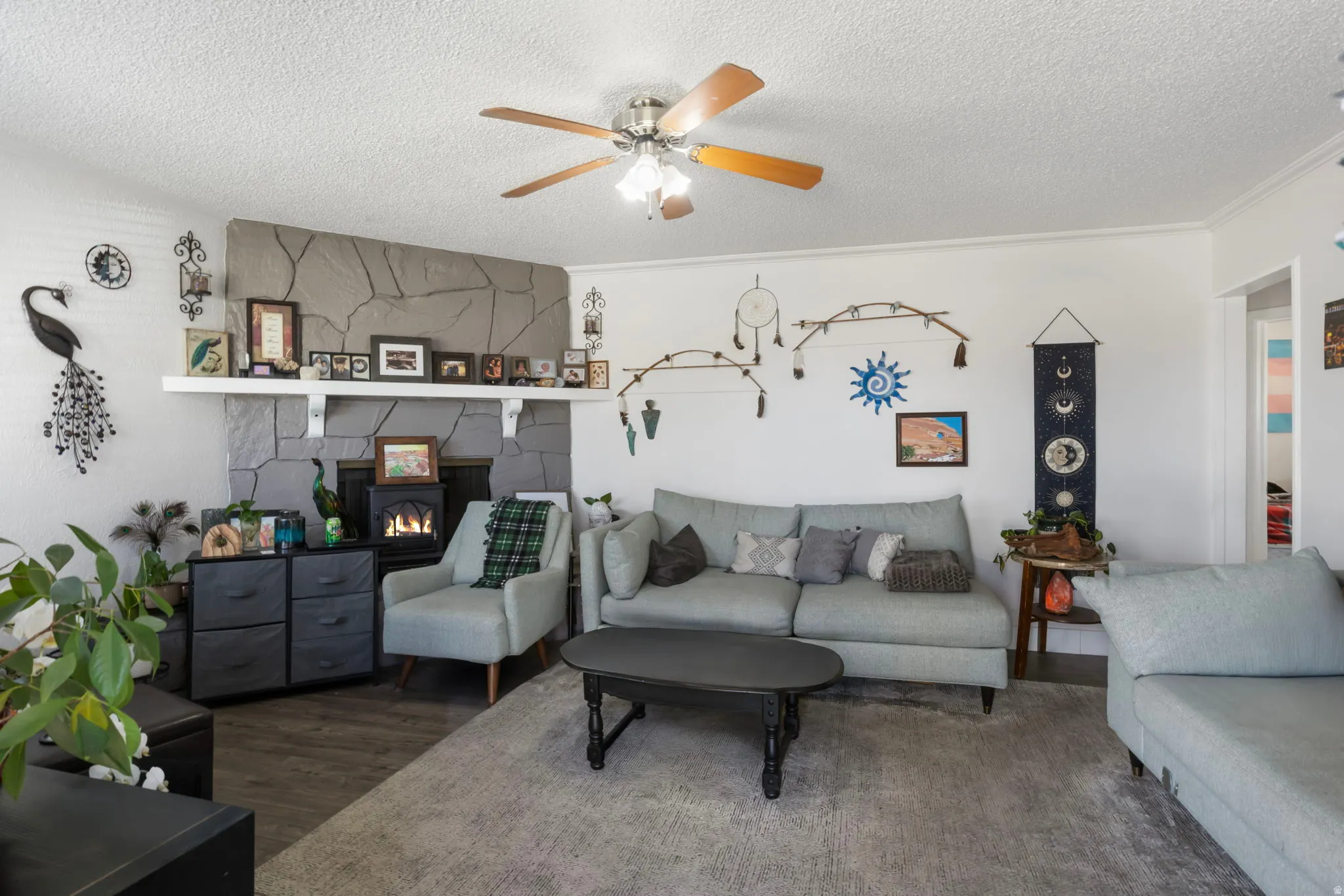Living room with ceiling fan, wood finished floors, a textured ceiling, and a lit fireplace